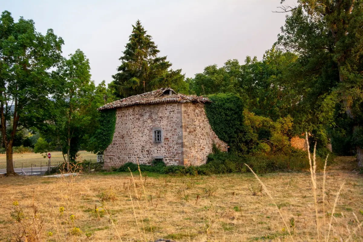 Ancienne bâtisse en pierre au toit de tuiles, entourée d'arbres, exemple de bâti à analyser avant tout projet