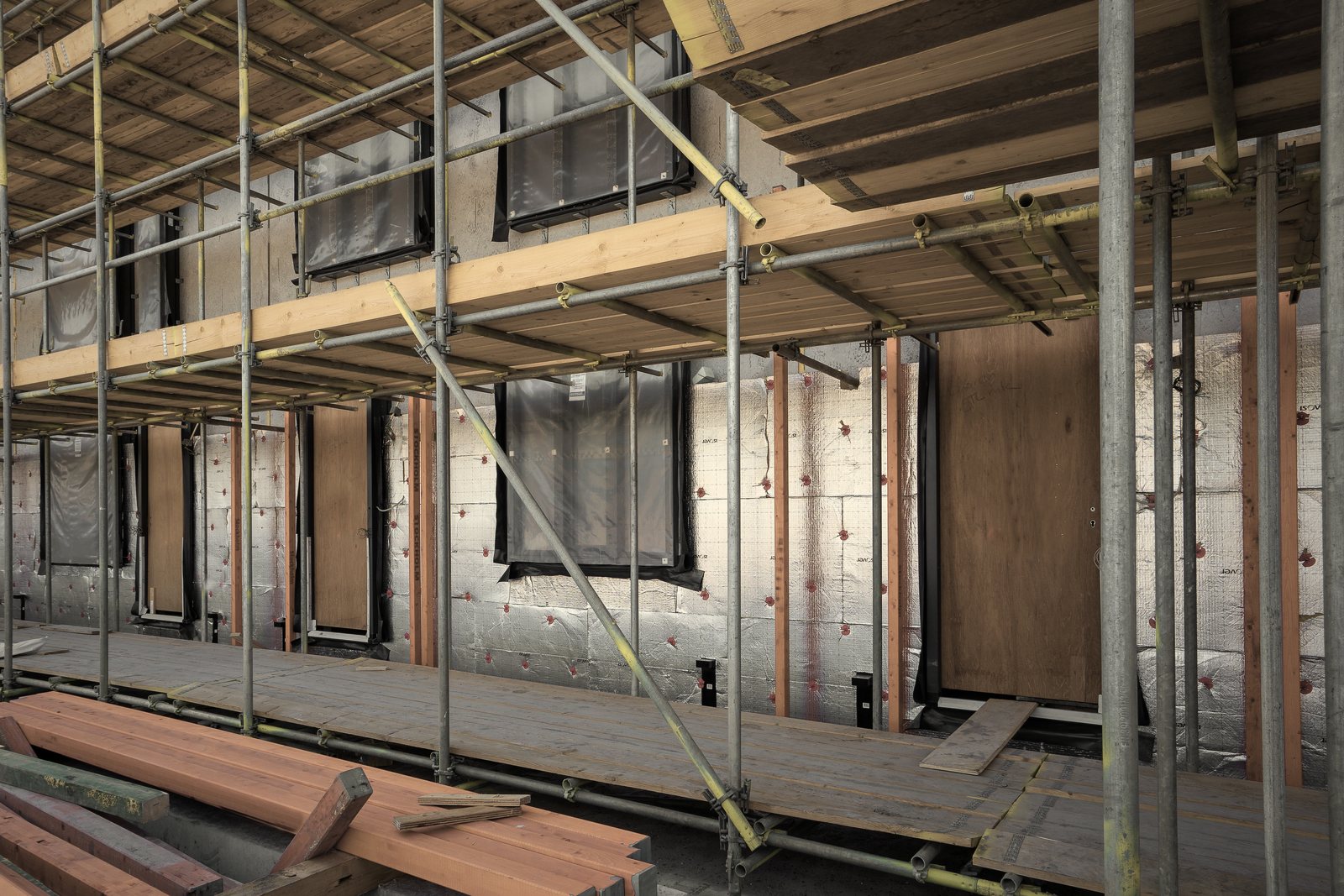 Façade en cours de travaux derrière un échafaudage, isolant posé et pièces de bois au sol, photo d'illustration
