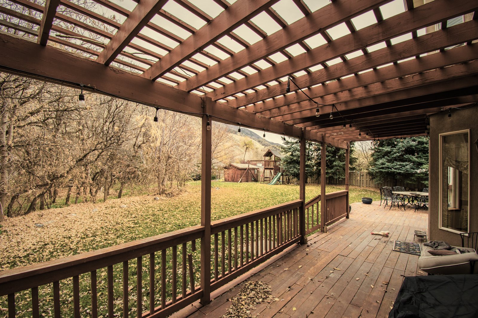 Terrasse en bois couverte d'une pergola à claire-voie, avec garde-corps en bois face au jardin, photo d'illustration