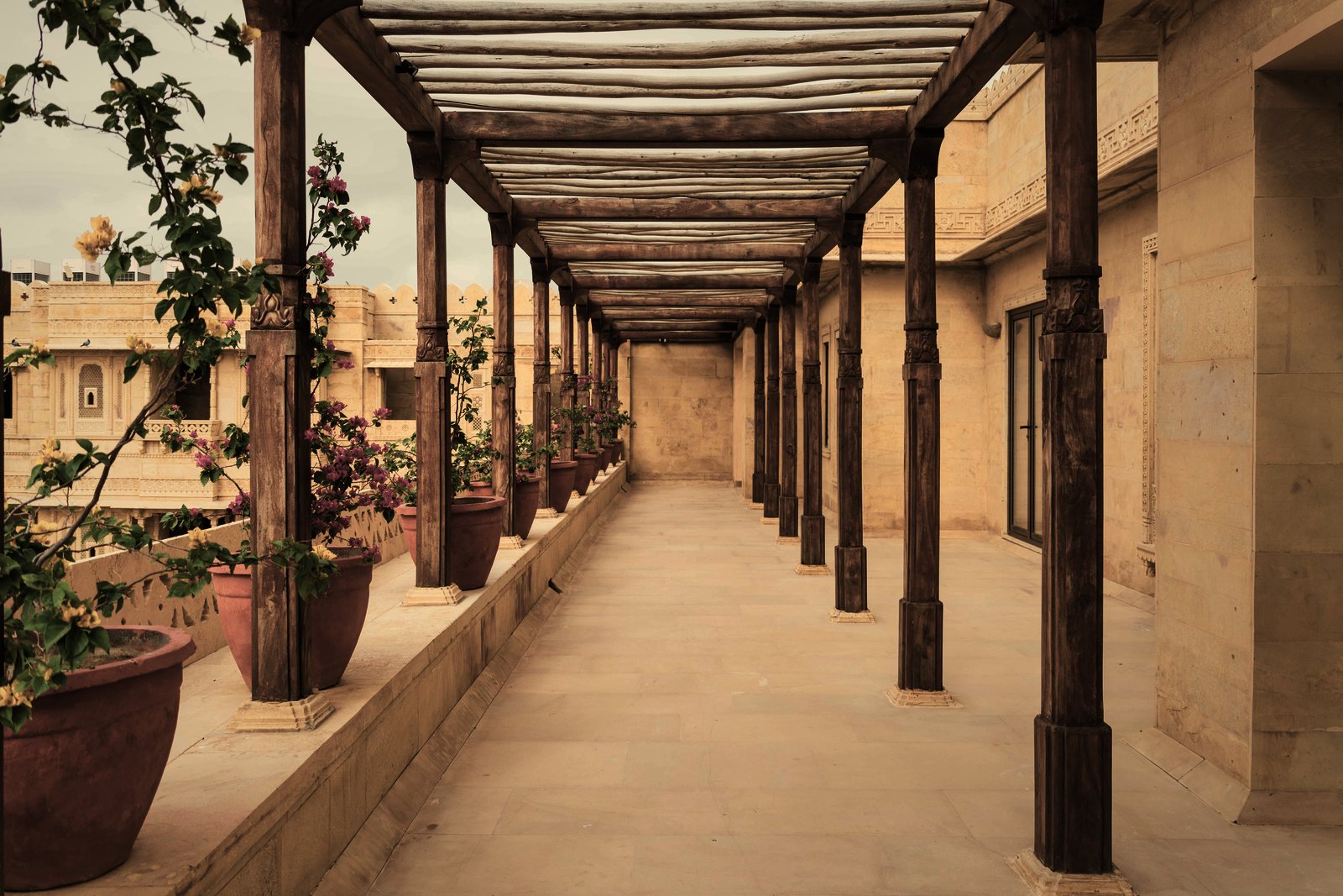 Galerie à poteaux et pergola en bois le long d'une façade en pierre de taille, pots de fleurs en terre cuite, photo d'illustration