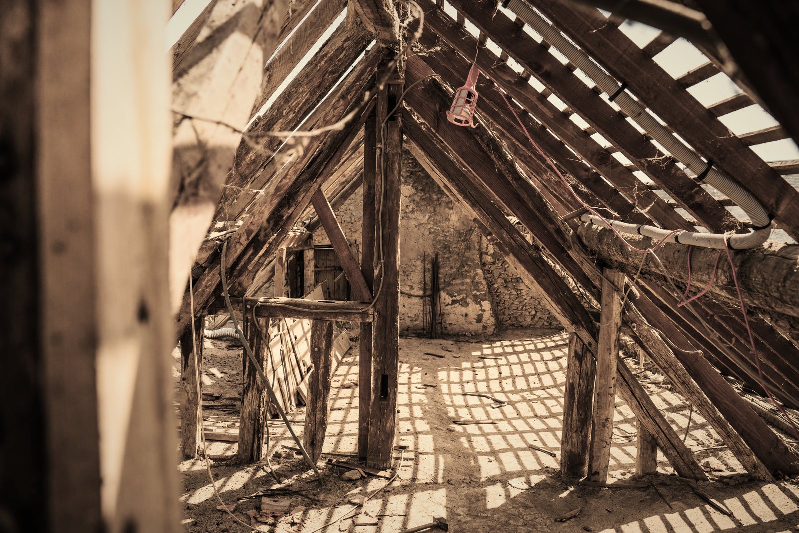 Charpente ancienne en bois dans un comble, traversée par la lumière passant entre les lattes, photo d'illustration