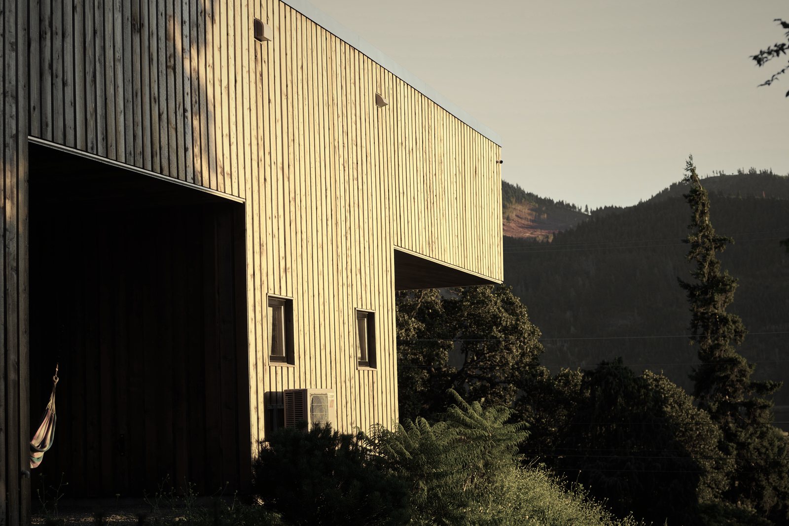Maison contemporaine à bardage de lames verticales en bois clair, face à des collines boisées, photo d'illustration