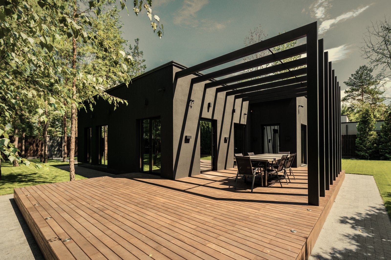 Maison contemporaine sombre prolongée par une pergola et une grande terrasse en bois, photo d'illustration