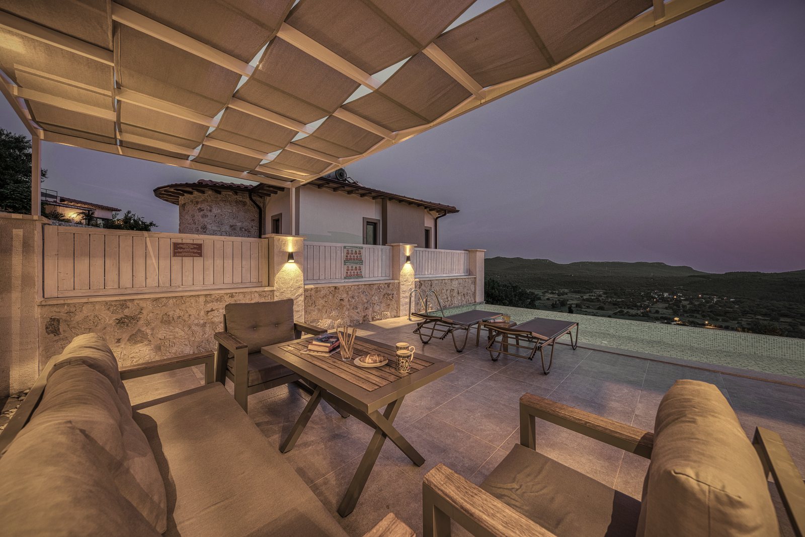 Terrasse couverte d'une toile tendue, face à une maison en pierre et aux collines au crépuscule, photo d'illustration