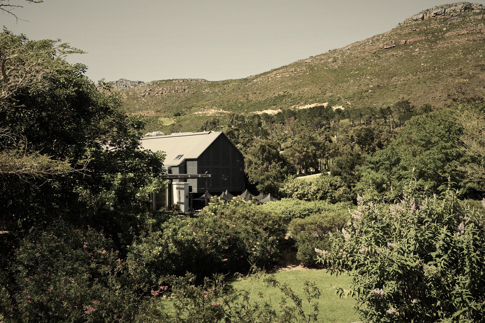 Maison contemporaine au toit sombre nichée dans la végétation, au pied d'une colline de garrigue, photo d'illustration