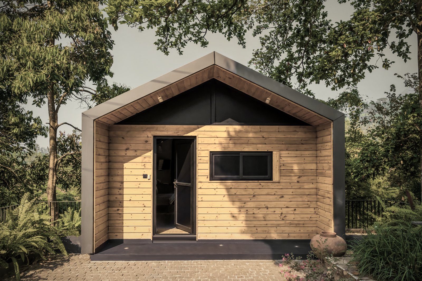 Petite maison à pignon habillée de lames de bois clair sous une toiture sombre, entre les arbres, photo d'illustration