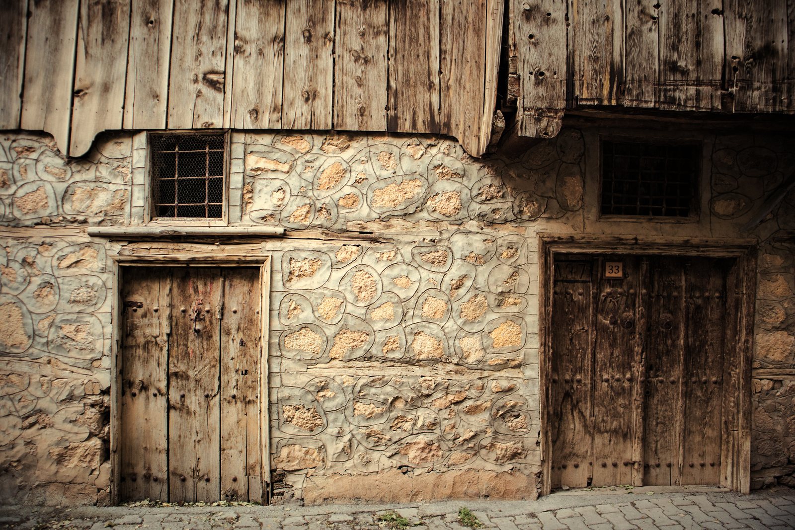 Rez-de-chaussée en moellons de pierre à portes en bois massif, surmonté d'un étage en planches, photo d'illustration