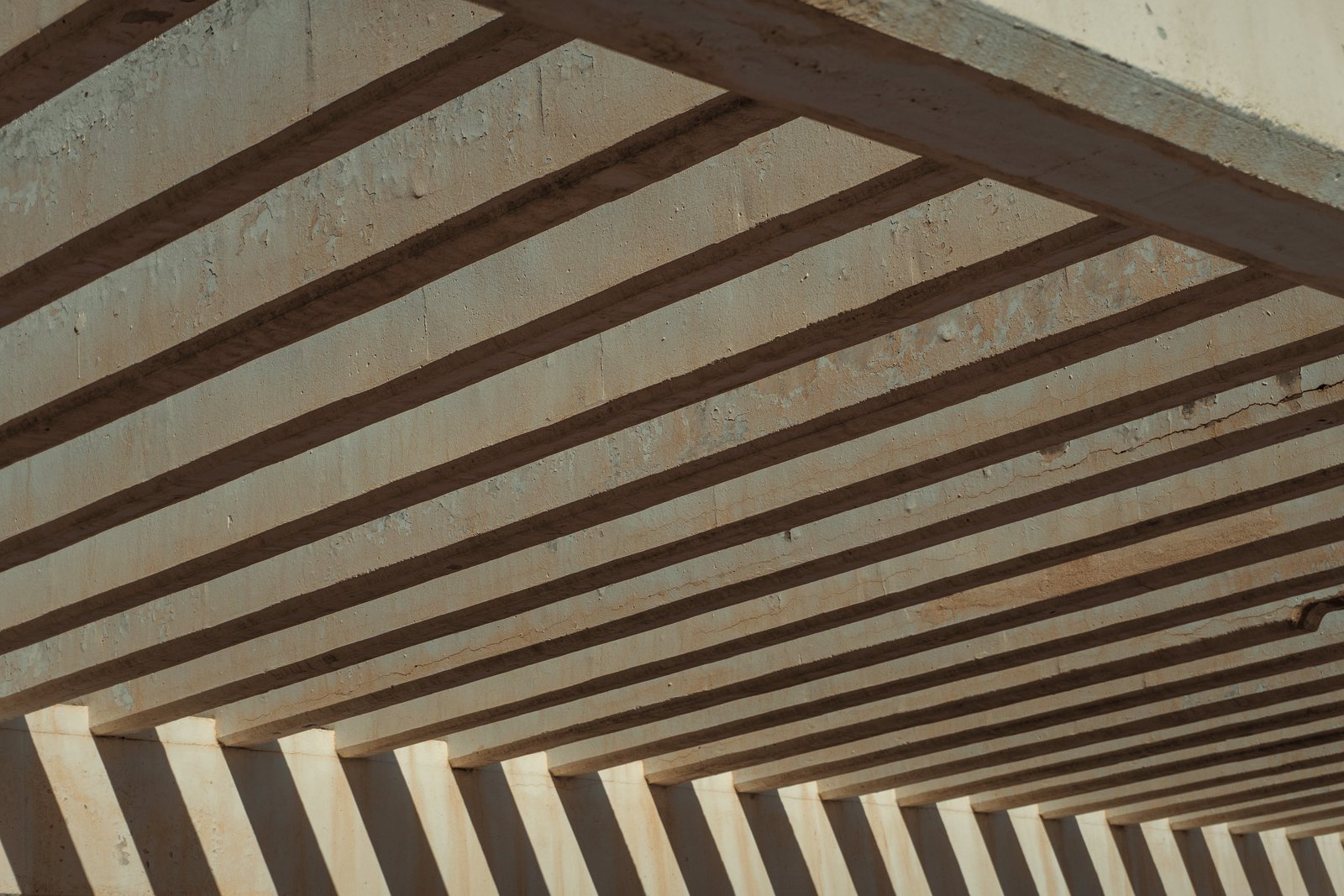 Pergola en poutres de bois clair qui projette une ombre rayée, vue d'en dessous, photo d'illustration