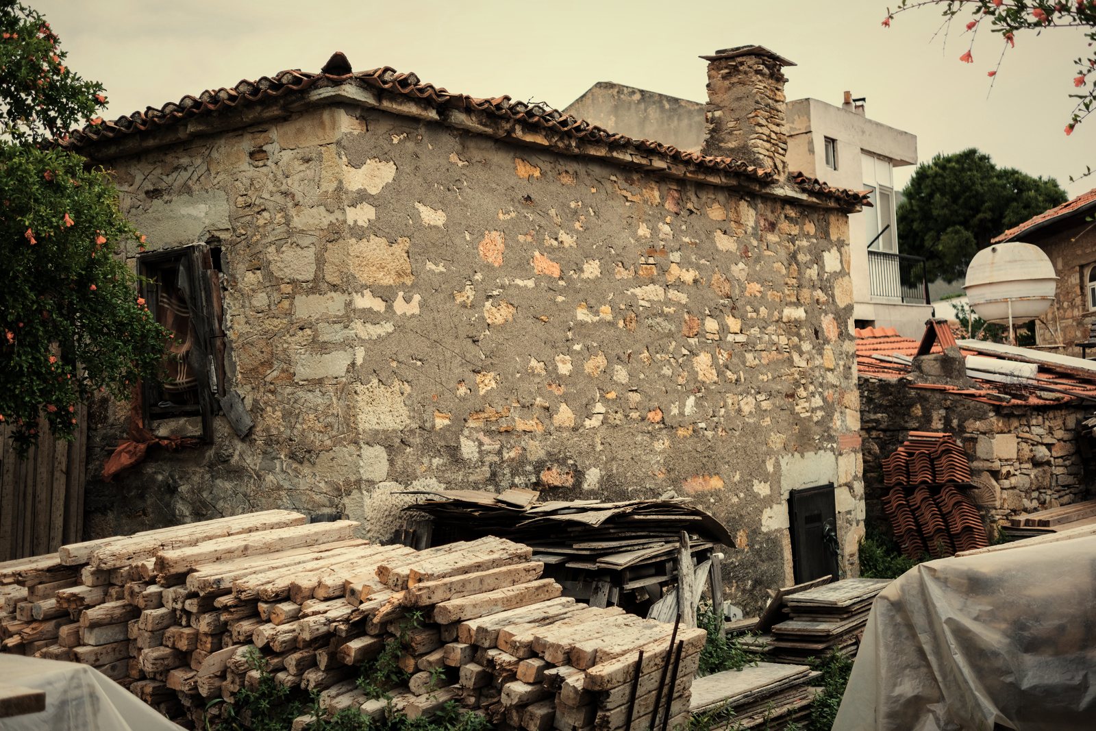 Maison en moellons de pierre à toiture en tuiles, avec des piles de bois de construction devant, photo d'illustration