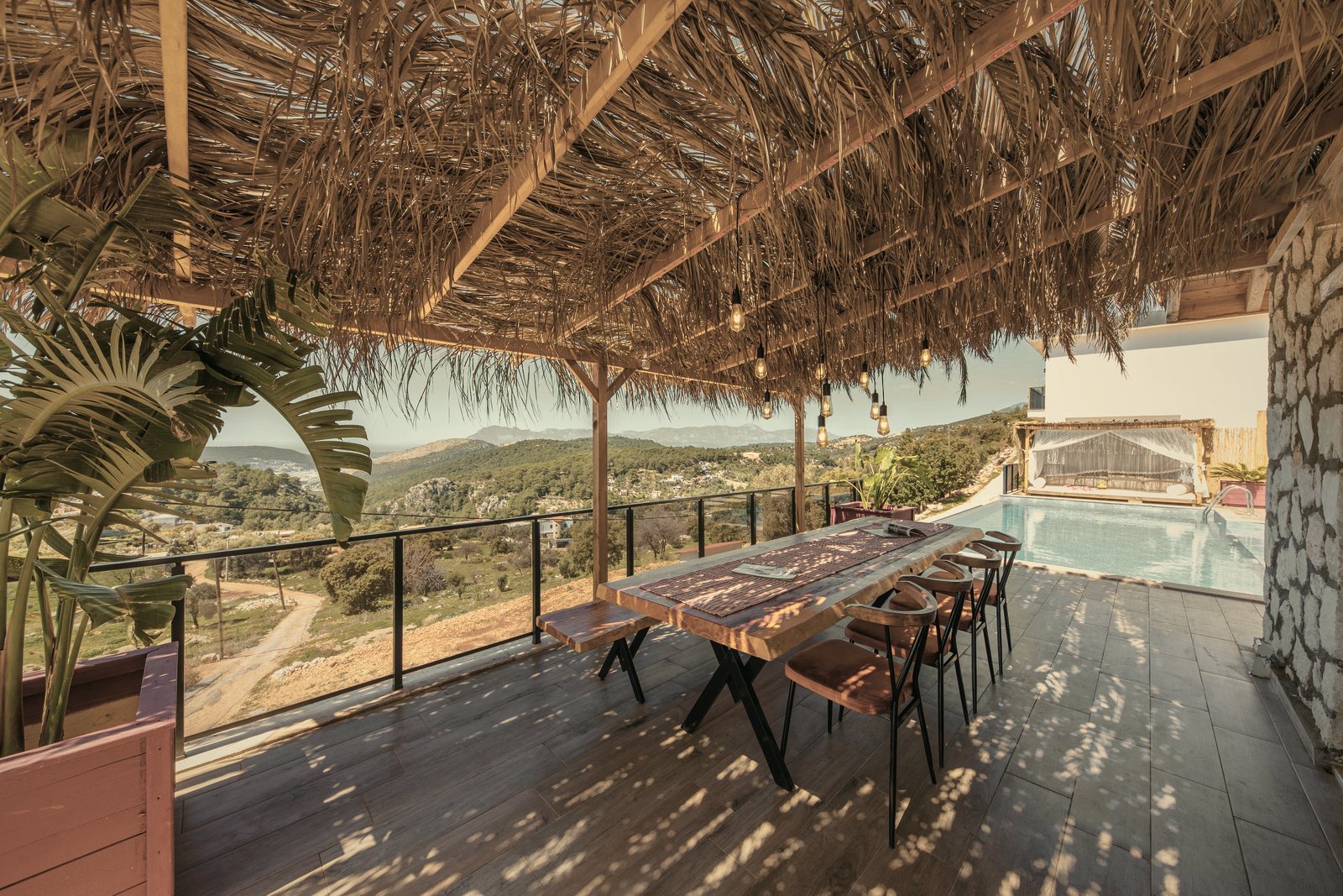 Terrasse en bois sous une couverture de roseaux, table en bois face aux collines et à une piscine, photo d'illustration