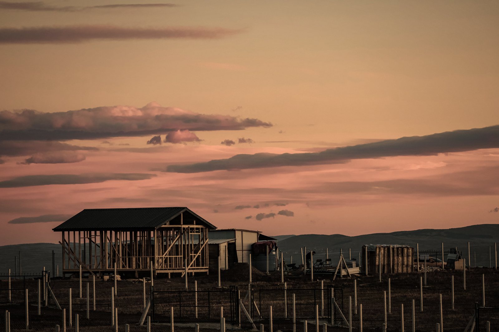 Ossature bois d'une maison en cours de montage sur un terrain, sous un ciel de coucher de soleil, photo d'illustration