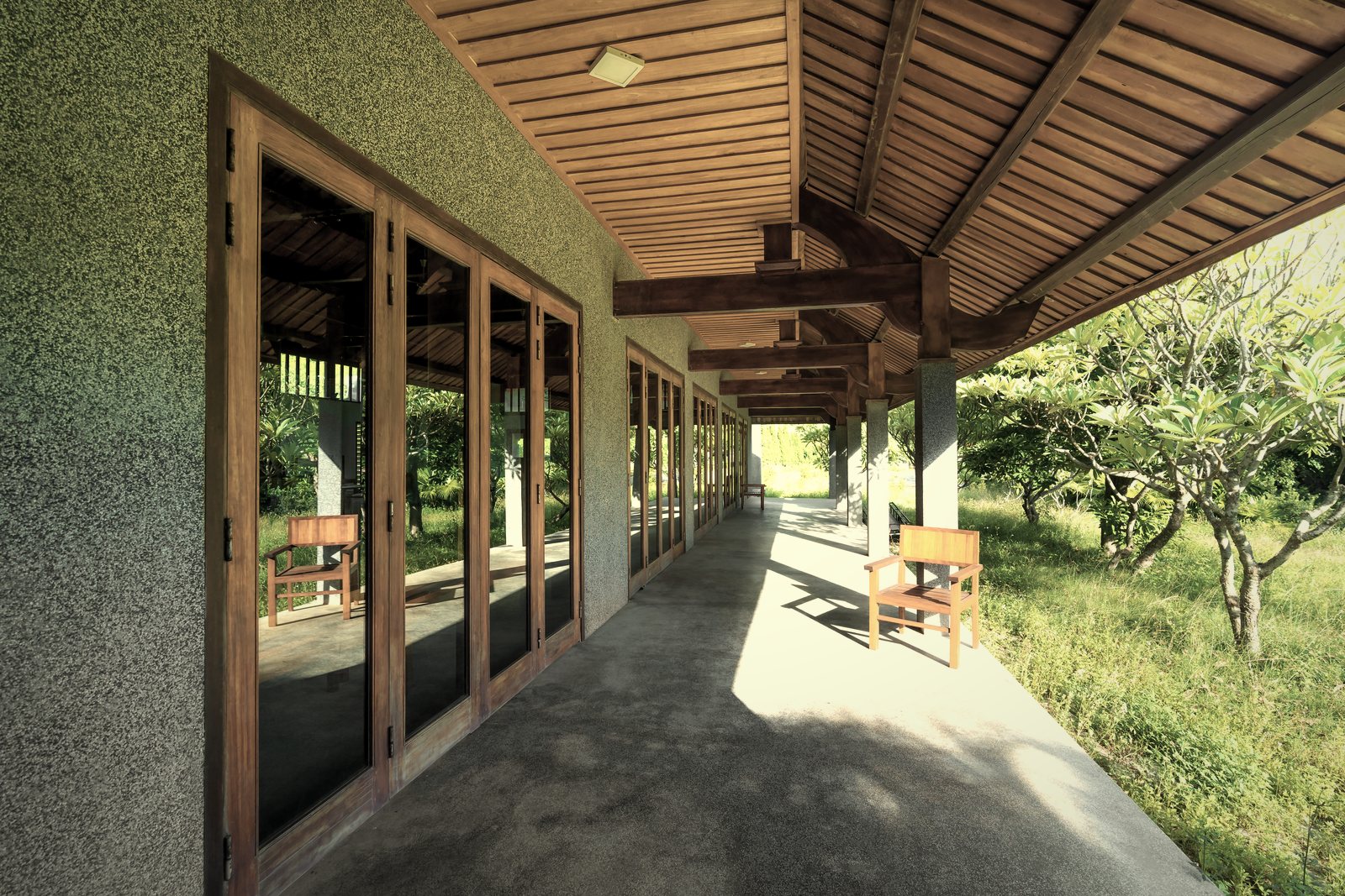 Galerie couverte par une charpente en bois le long d'une maison enduite aux menuiseries bois, photo d'illustration