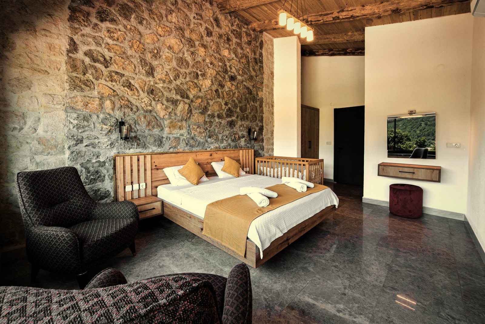 Chambre au mur en moellons de pierre apparents sous un plafond en bois, lit en bois clair, photo d'illustration