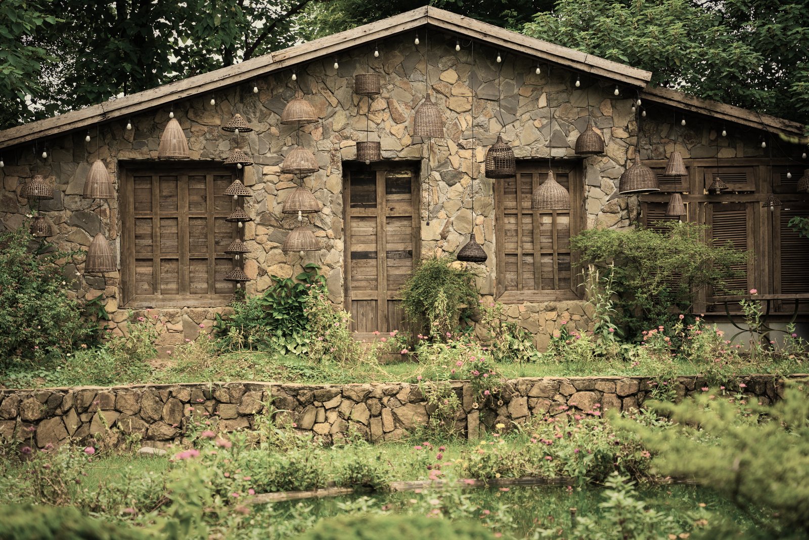 Maison en pierre aux fenêtres et portes en bois, précédée d'un jardin fleuri et d'un muret, photo d'illustration