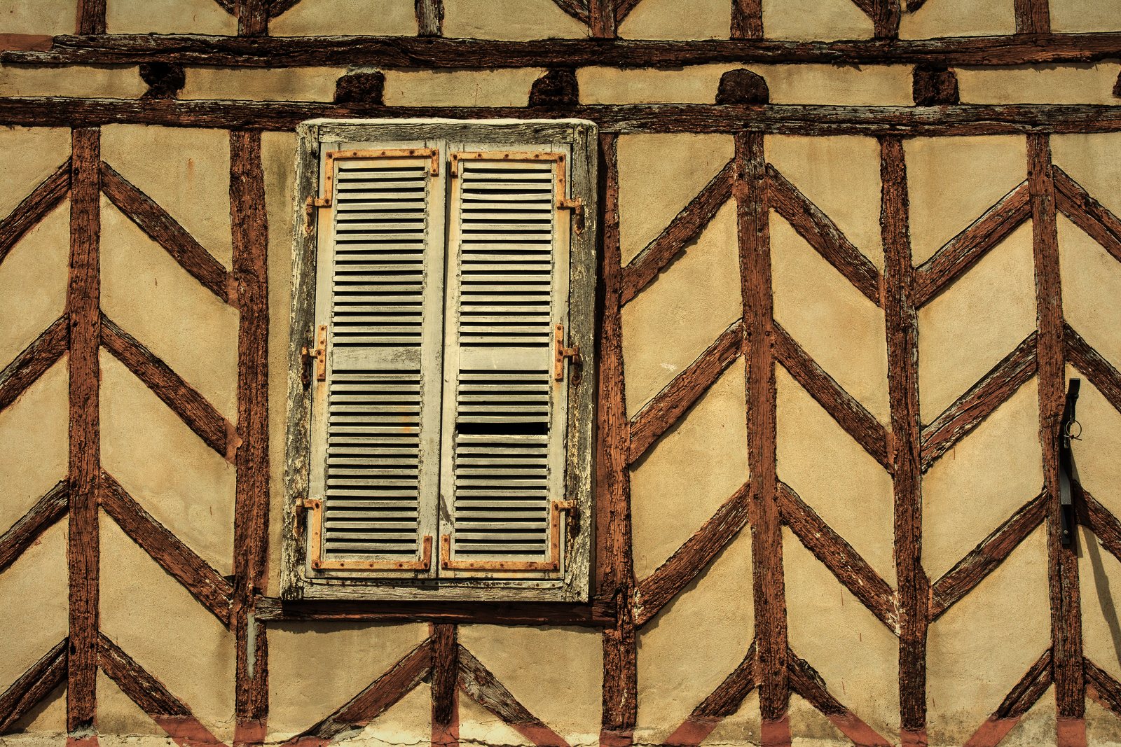 Façade à pans de bois en chevrons remplis d'enduit clair, autour d'une fenêtre à persiennes, photo d'illustration