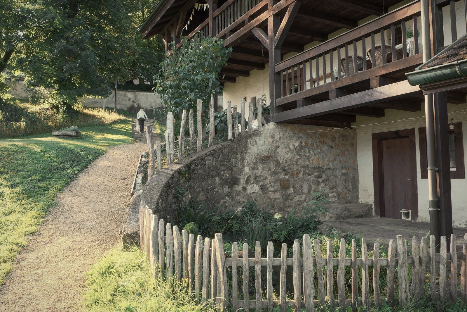 Maison à soubassement en pierre et galerie en bois à l'étage, près d'un chemin et d'une clôture en bois, photo d'illustration