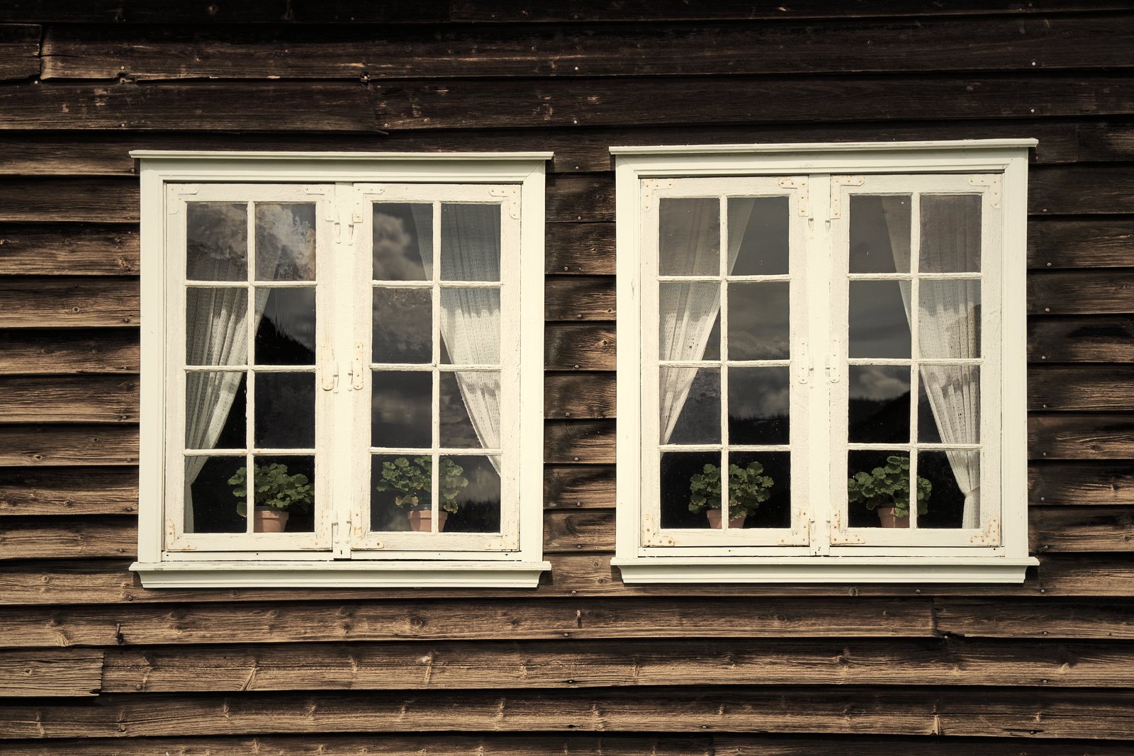 Façade en bardage de bois sombre percée de deux fenêtres blanches à petits carreaux, photo d'illustration