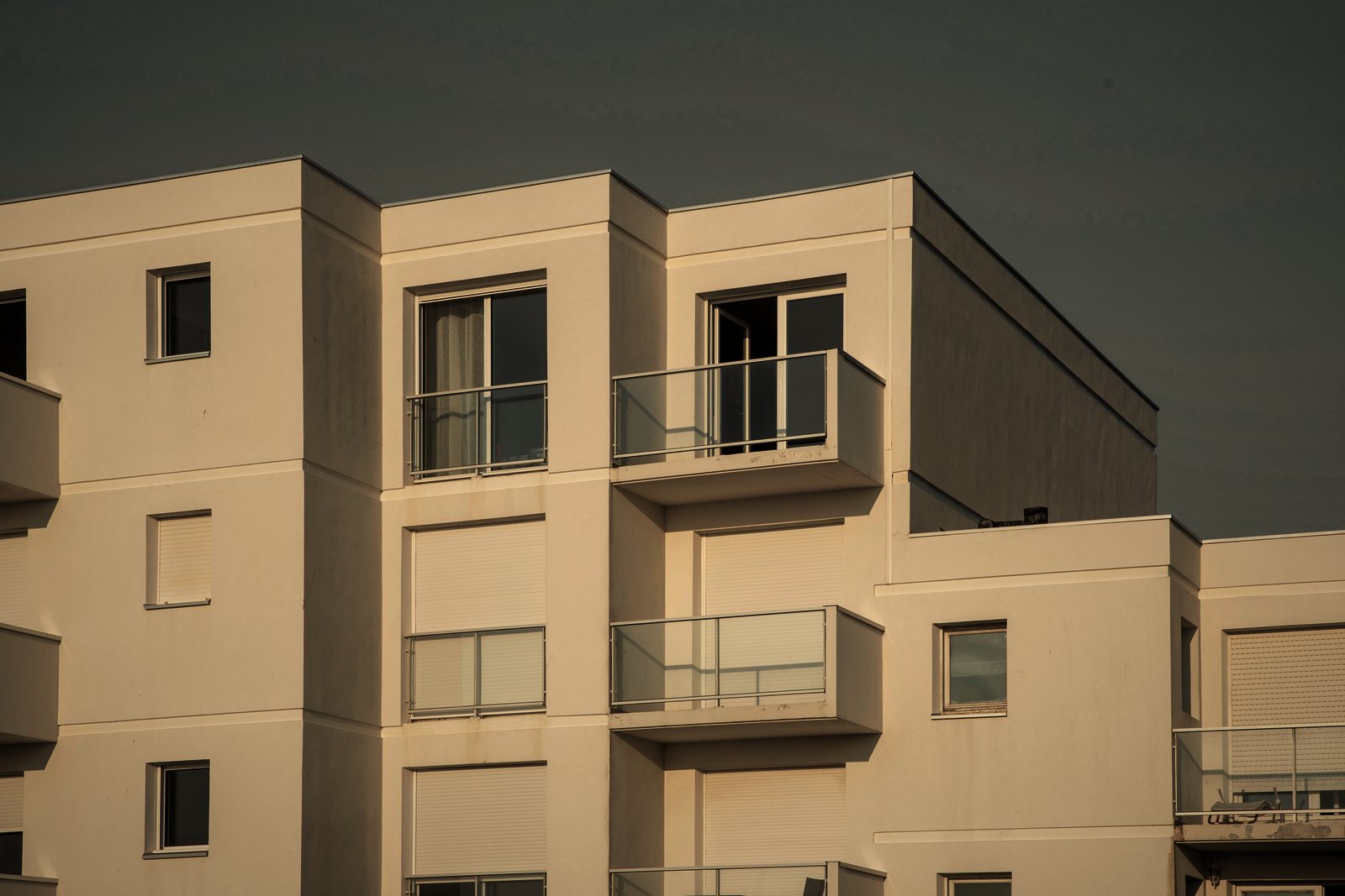 Petit immeuble de logements à façade claire enduite, balcons à garde-corps métalliques et volumes en décrochés, photo d'illustration
