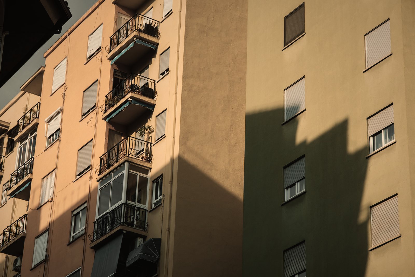 Façade d'immeuble d'habitation ocre à balcons superposés et volets roulants, ombre portée d'un bâtiment voisin, photo d'illustration