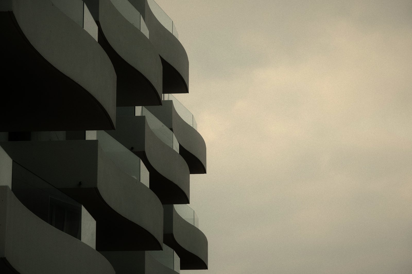 Balcons courbes superposés en gradins sur un immeuble blanc, sous un ciel gris, photo d'illustration