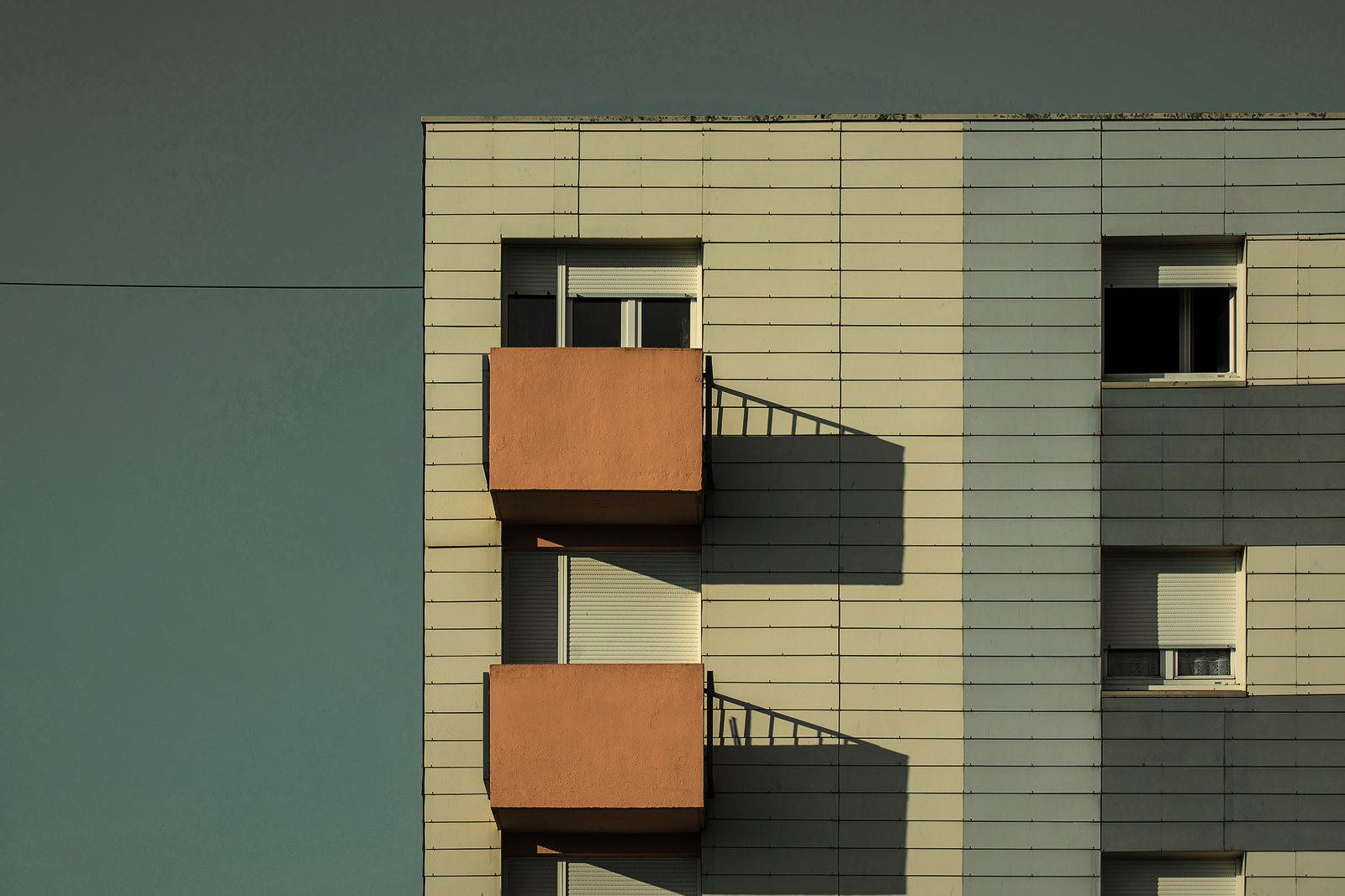 Balcons en saillie orangés sur une façade à bardage clair, avec leur ombre portée, photo d'illustration