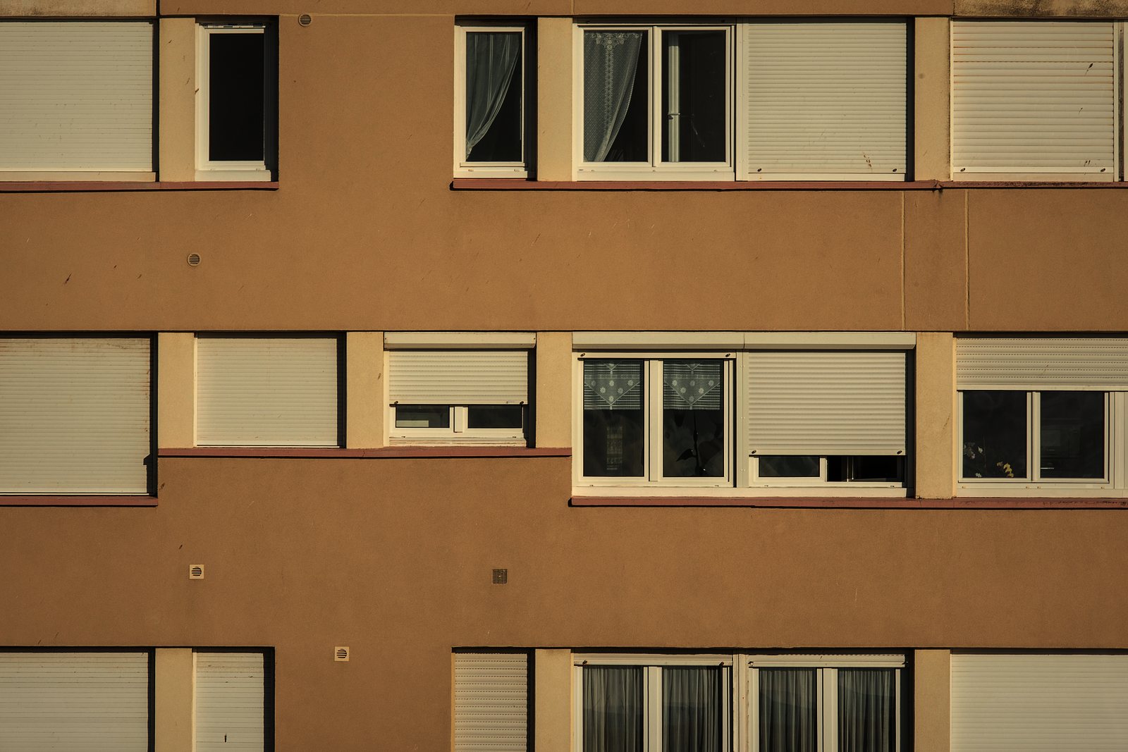 Façade enduite d'un immeuble des années 1960, fenêtres à volets roulants et bandeaux horizontaux, photo d'illustration