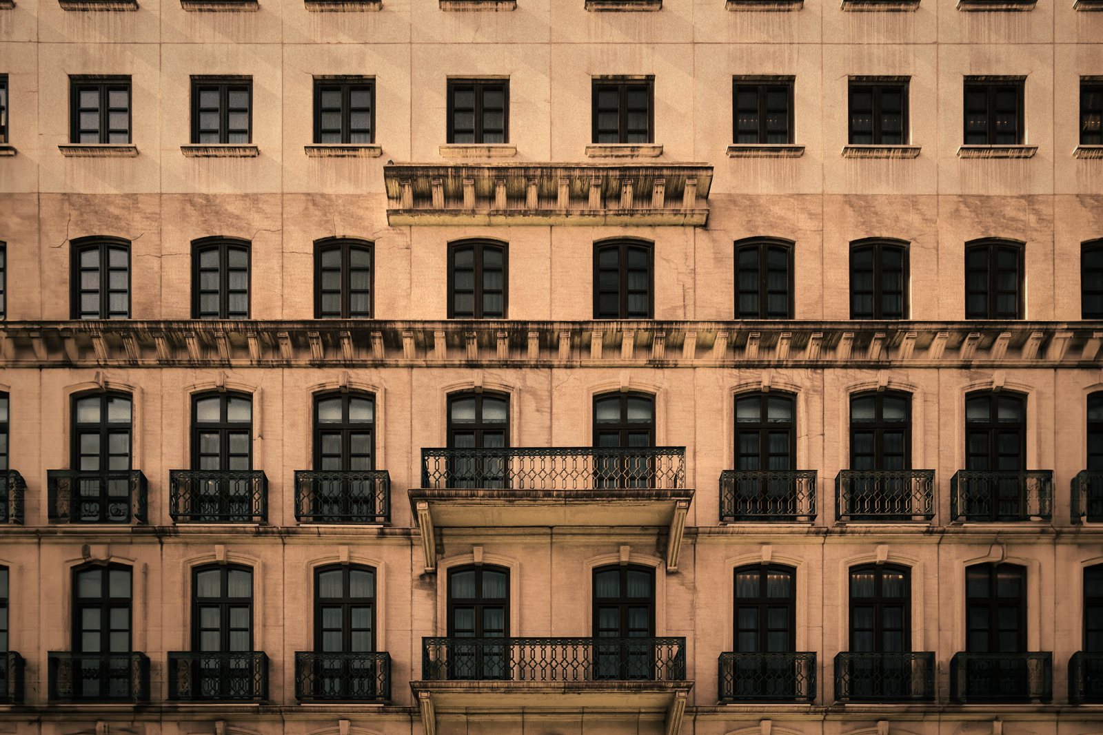 Grande façade ancienne rose à fenêtres régulières et balcons en fer forgé superposés, photo d'illustration