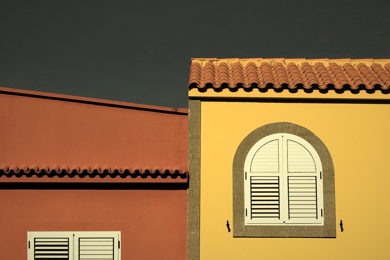 Façades enduites ocre rouge et jaune sous des rives de tuiles canal, fenêtre cintrée à volets, photo d'illustration