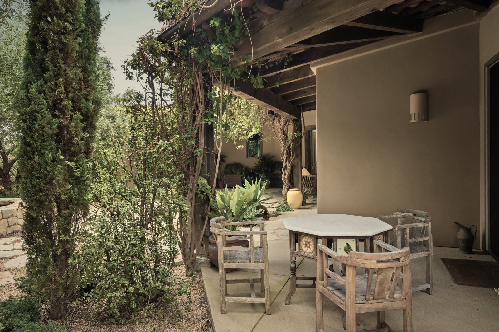 Terrasse couverte d'une pergola en bois, table et chaises, cyprès et plantes méditerranéennes, photo d'illustration