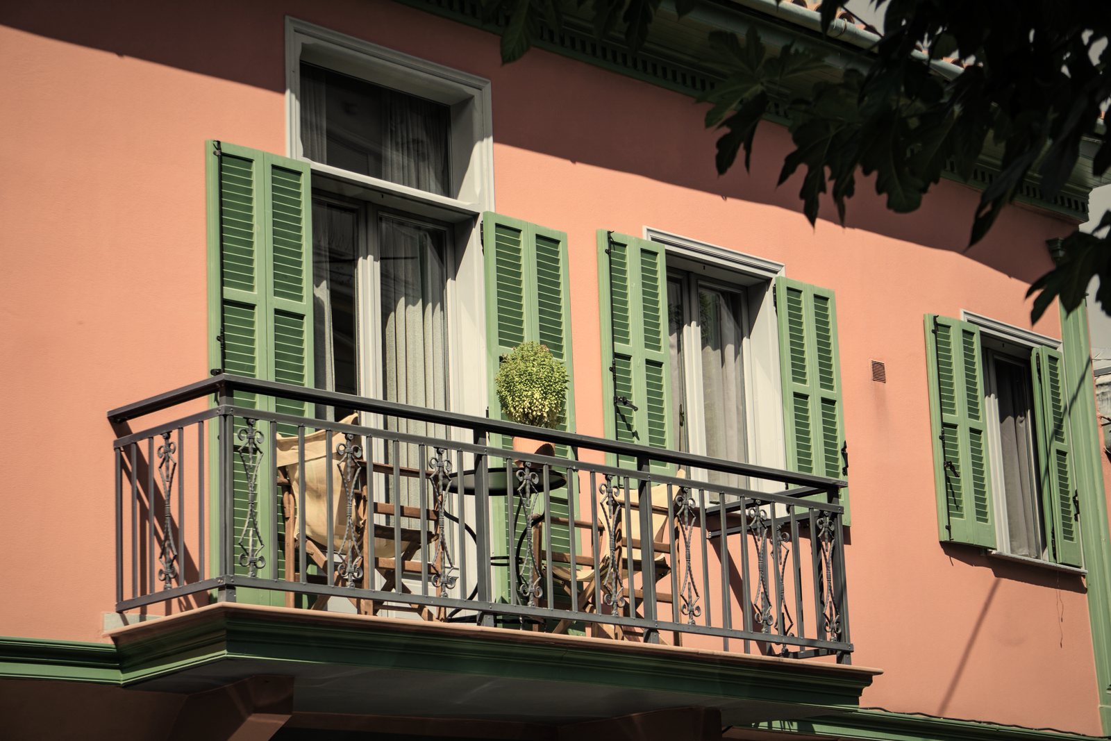 Balcon en fer forgé devant des portes-fenêtres à volets verts, façade enduite rose, photo d'illustration