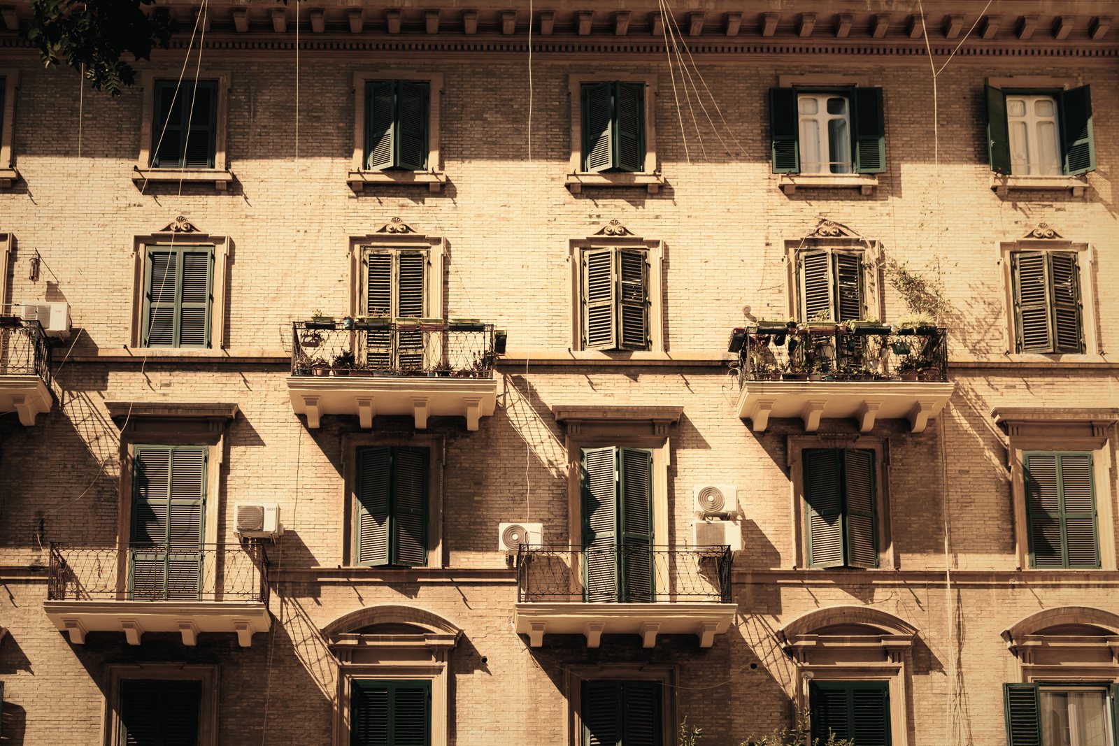 Façade ancienne en brique et enduit rosé à volets verts, balconnets et climatiseurs, photo d'illustration