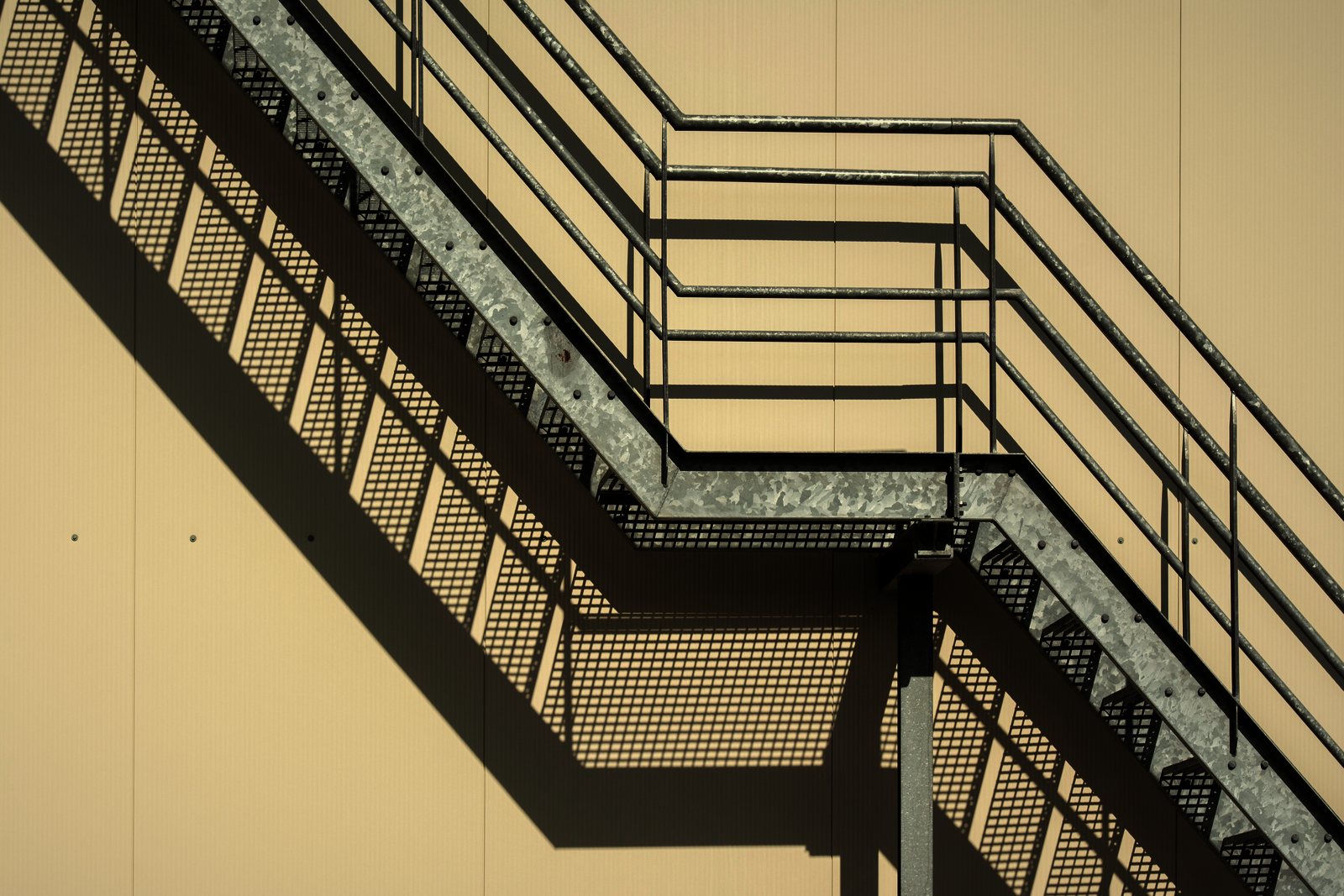 Escalier extérieur métallique en acier galvanisé fixé sur une façade beige, ombres rasantes, photo d'illustration