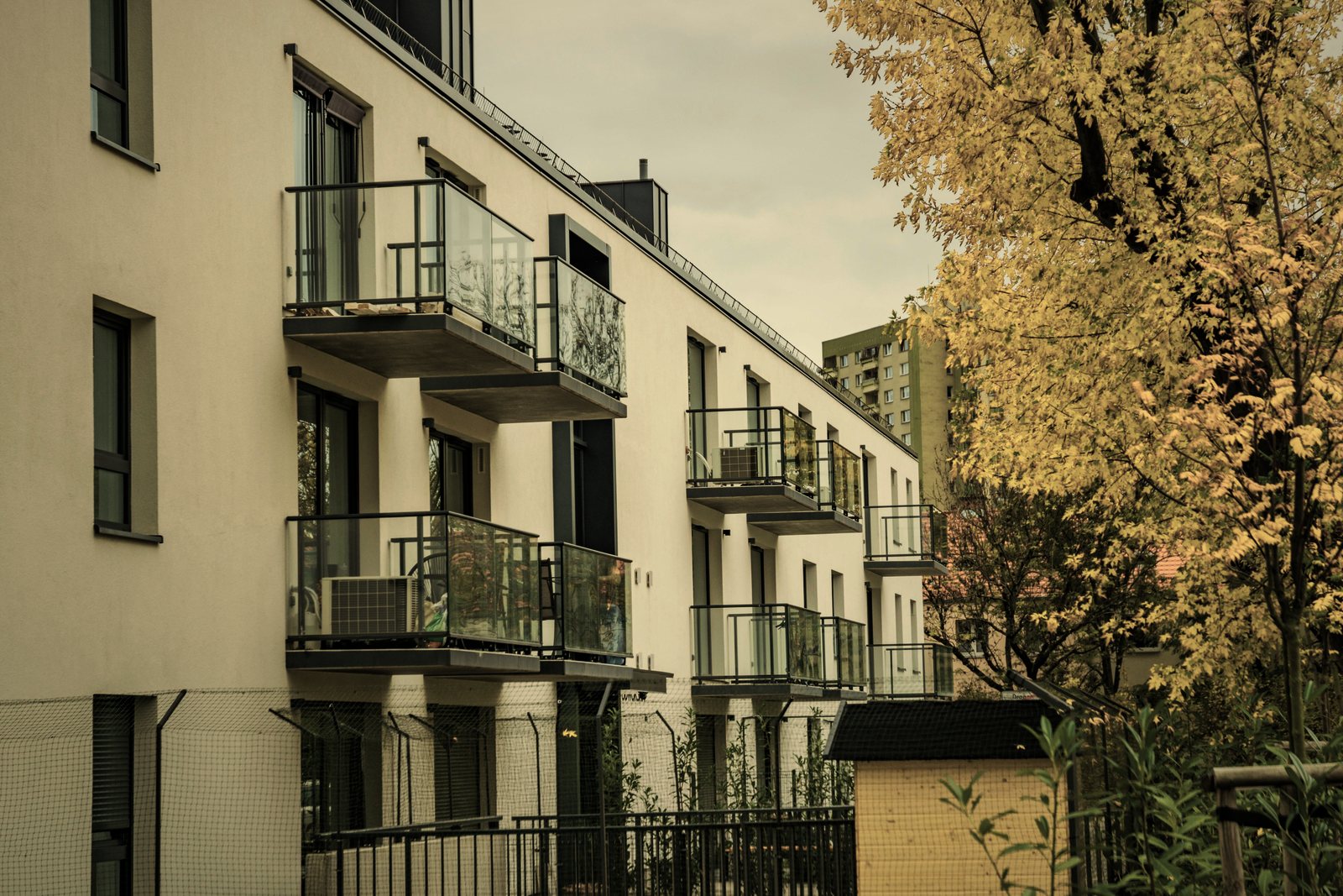 Immeuble résidentiel à façade claire et balcons à garde-corps vitrés, arbre aux feuilles d'automne, photo d'illustration