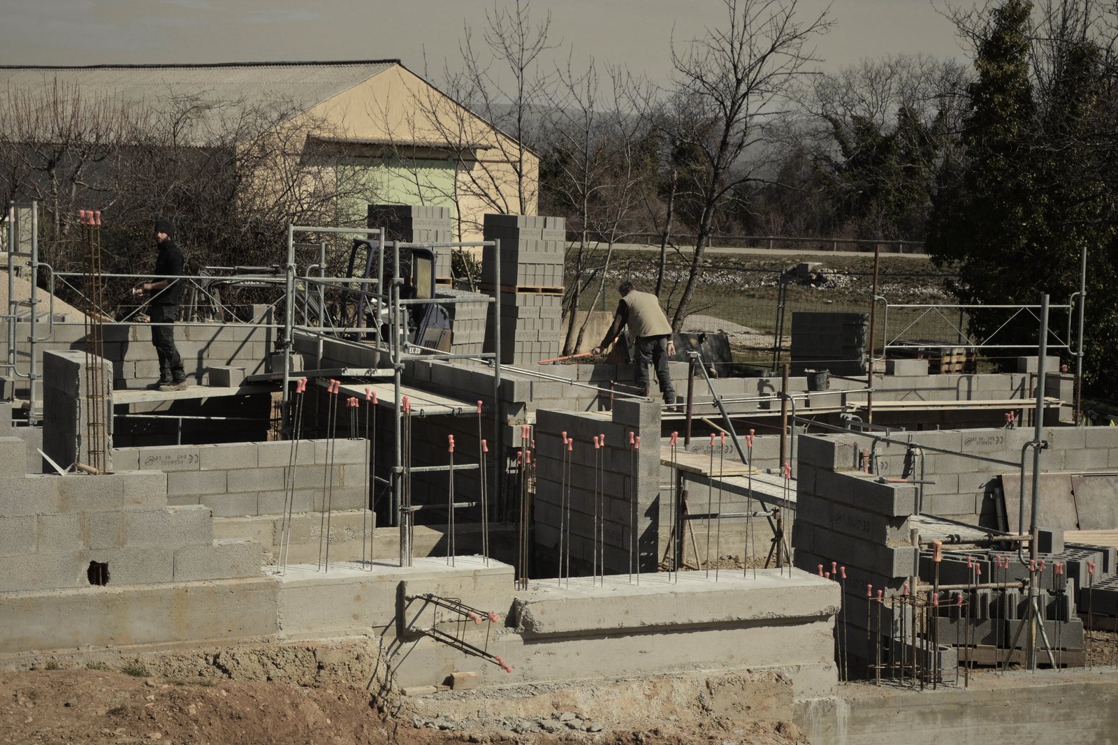 Élévation de murs en blocs béton sur le chantier d'un petit bâtiment, échafaudage et maçons au loin, photo d'illustration