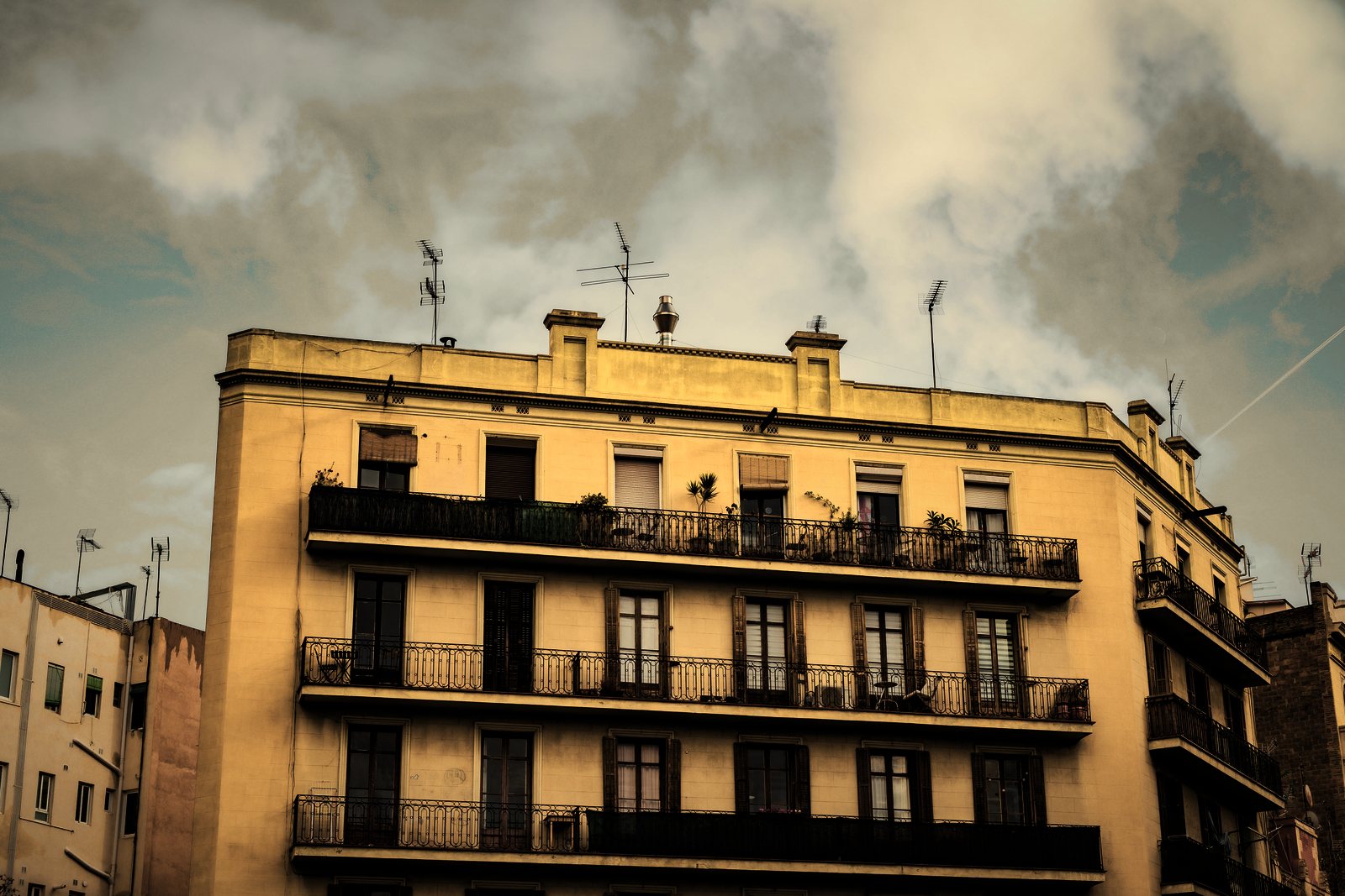 Angle d'immeuble ancien à enduit jaune et balcons filants en fer forgé sur trois niveaux, photo d'illustration