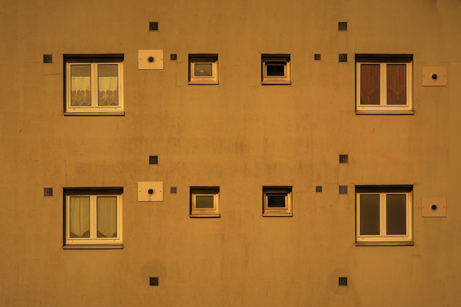 Façade enduite ocre jaune d'un immeuble d'habitation, fenêtres régulières et petites baies de ventilation, photo d'illustration