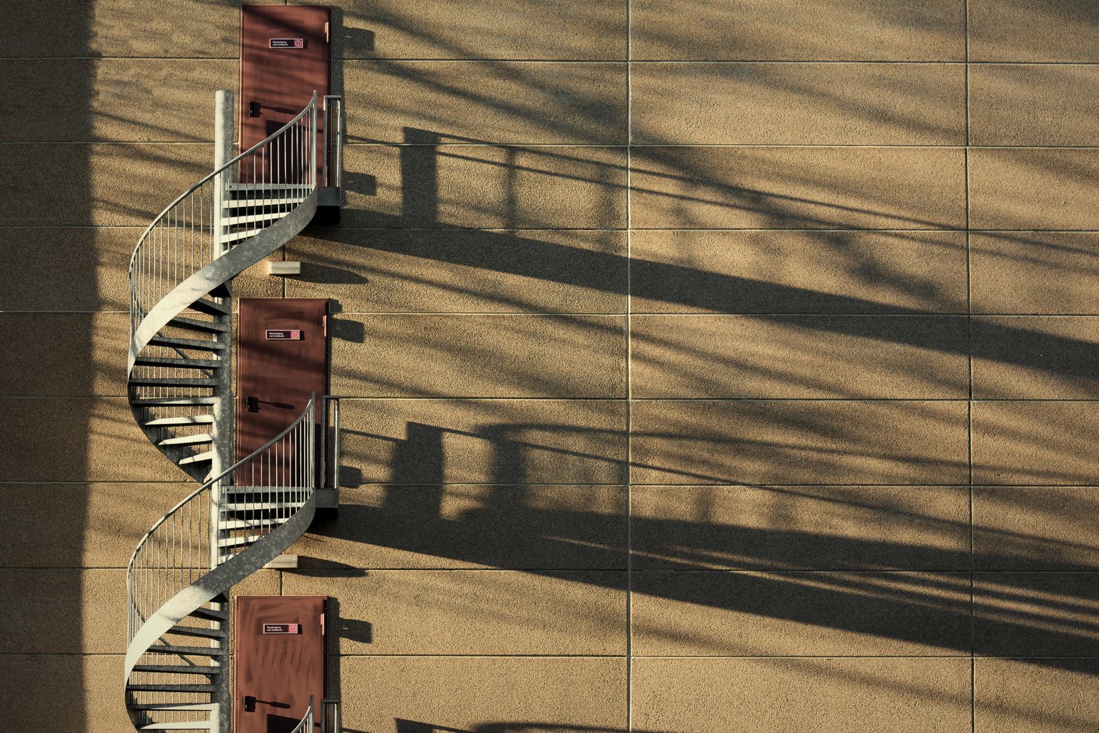 Escalier hélicoïdal métallique desservant des portes sur une façade beige, ombres portées, photo d'illustration