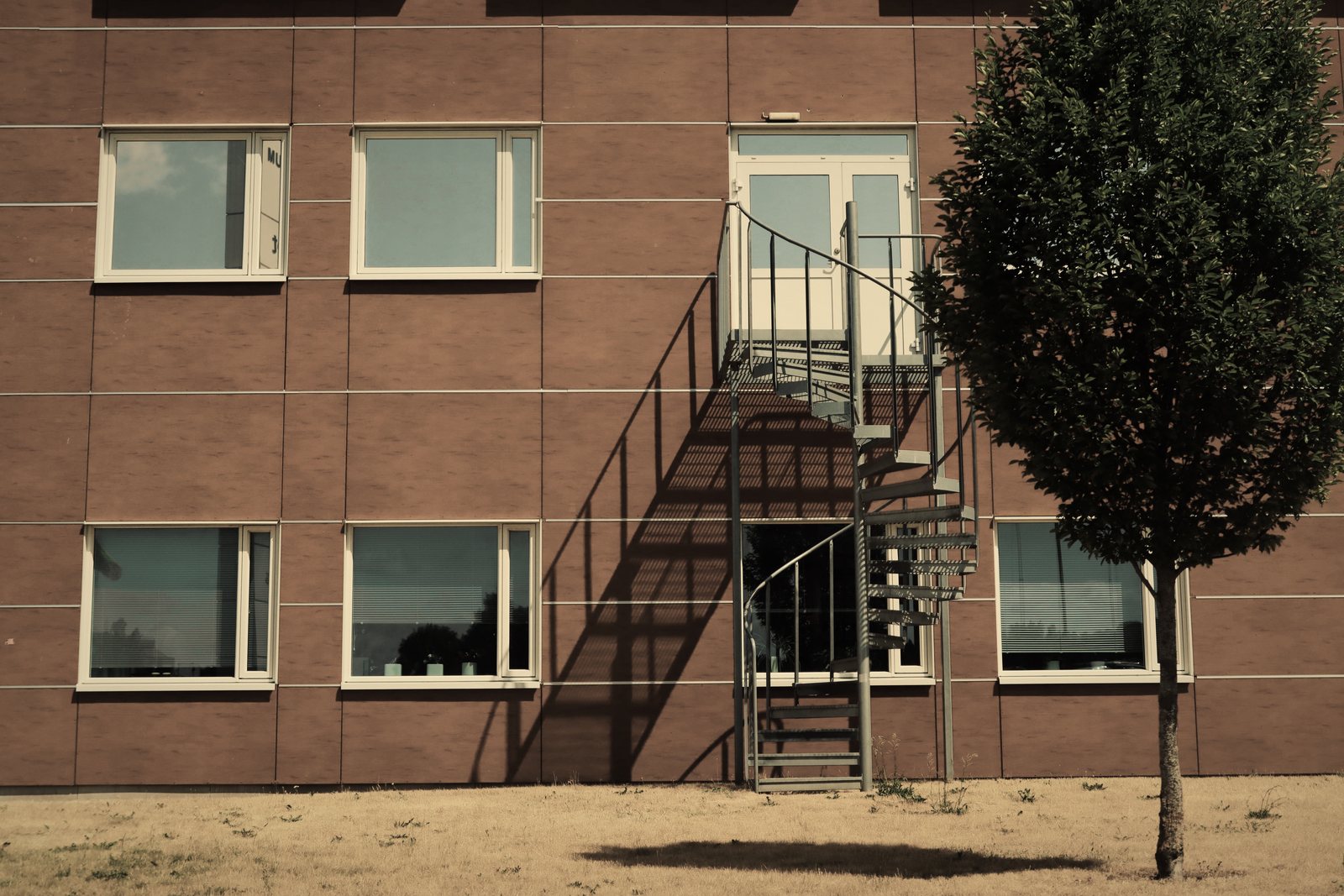 Escalier hélicoïdal métallique accolé à une façade en brique rouge, arbre isolé devant, photo d'illustration