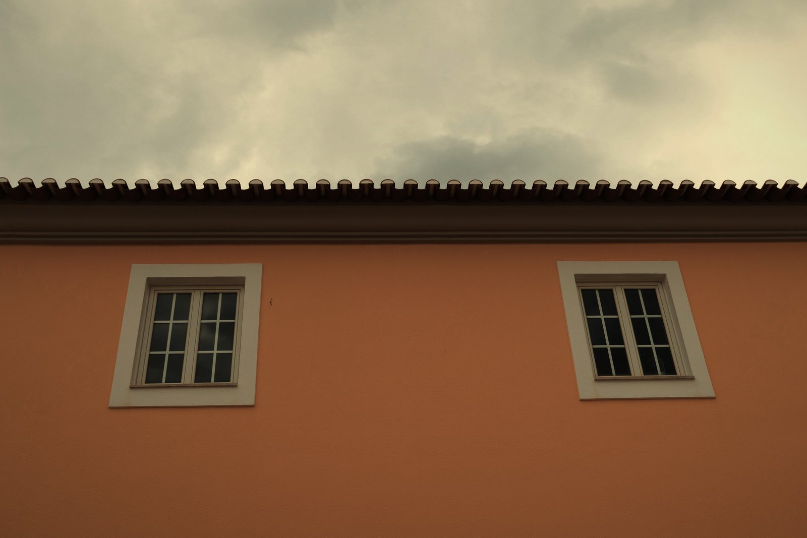 Façade enduite saumon sous génoise et débord de toit en tuiles, deux fenêtres blanches, photo d'illustration