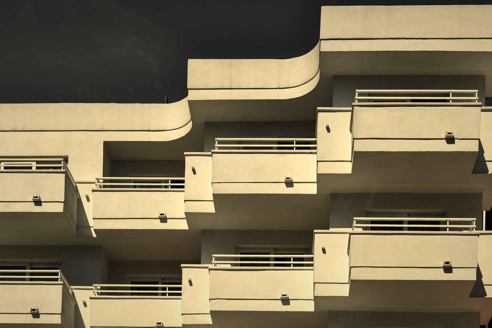 Terrasses courbes superposées et décalées sur un immeuble blanc, garde-corps métalliques, photo d'illustration