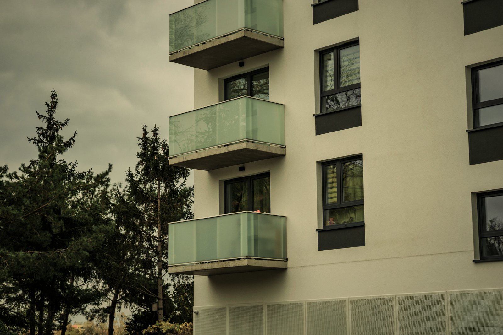 Façade blanche d'immeuble de logements à balcons en verre dépoli, conifères au premier plan, photo d'illustration