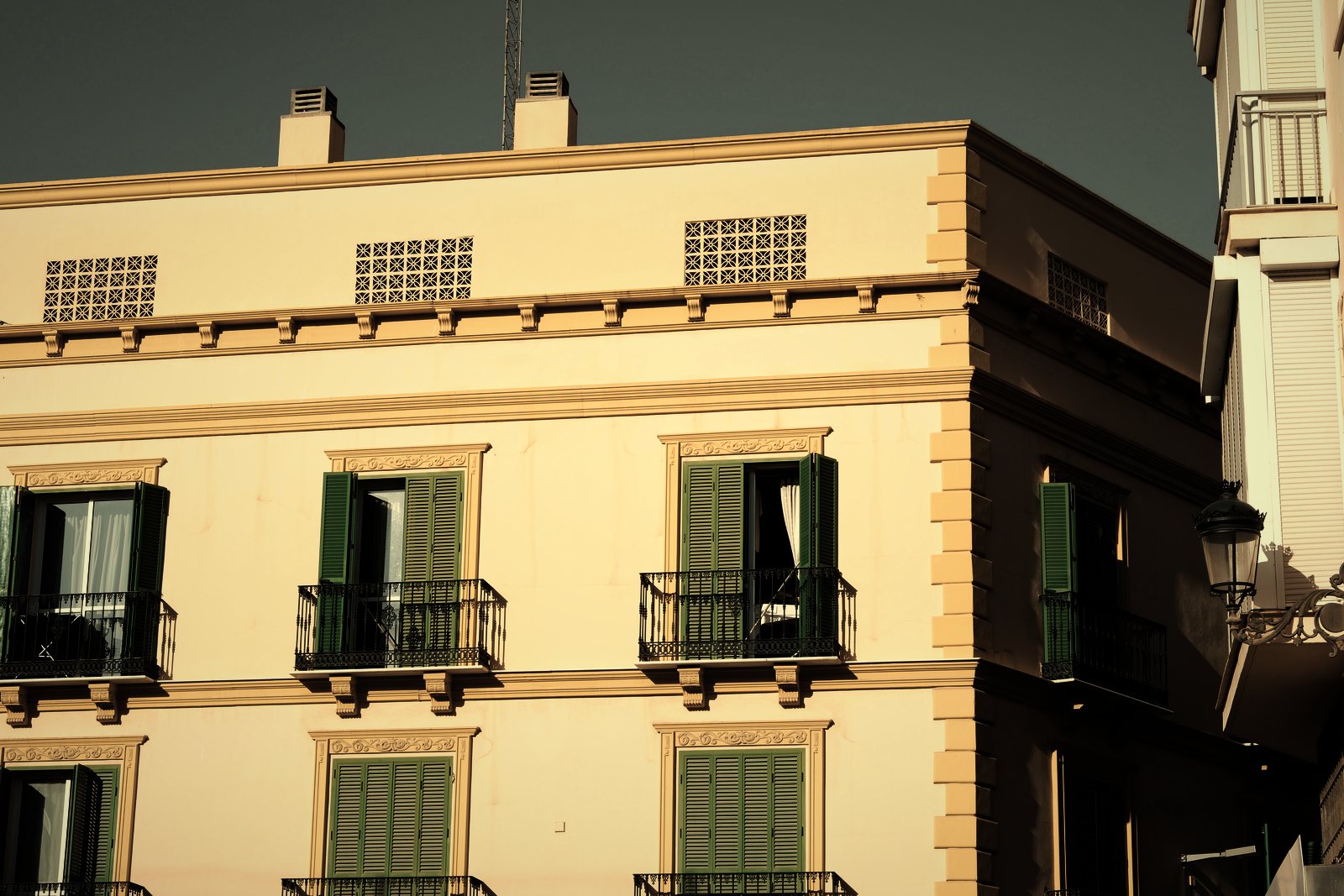 Angle d'immeuble ancien à façade crème, volets verts et balconnets en fer forgé, photo d'illustration