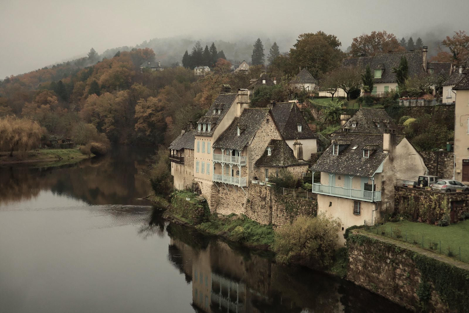 Maisons en pierre à toits d'ardoise au bord d'une rivière, colline boisée dans la brume, photo d'illustration