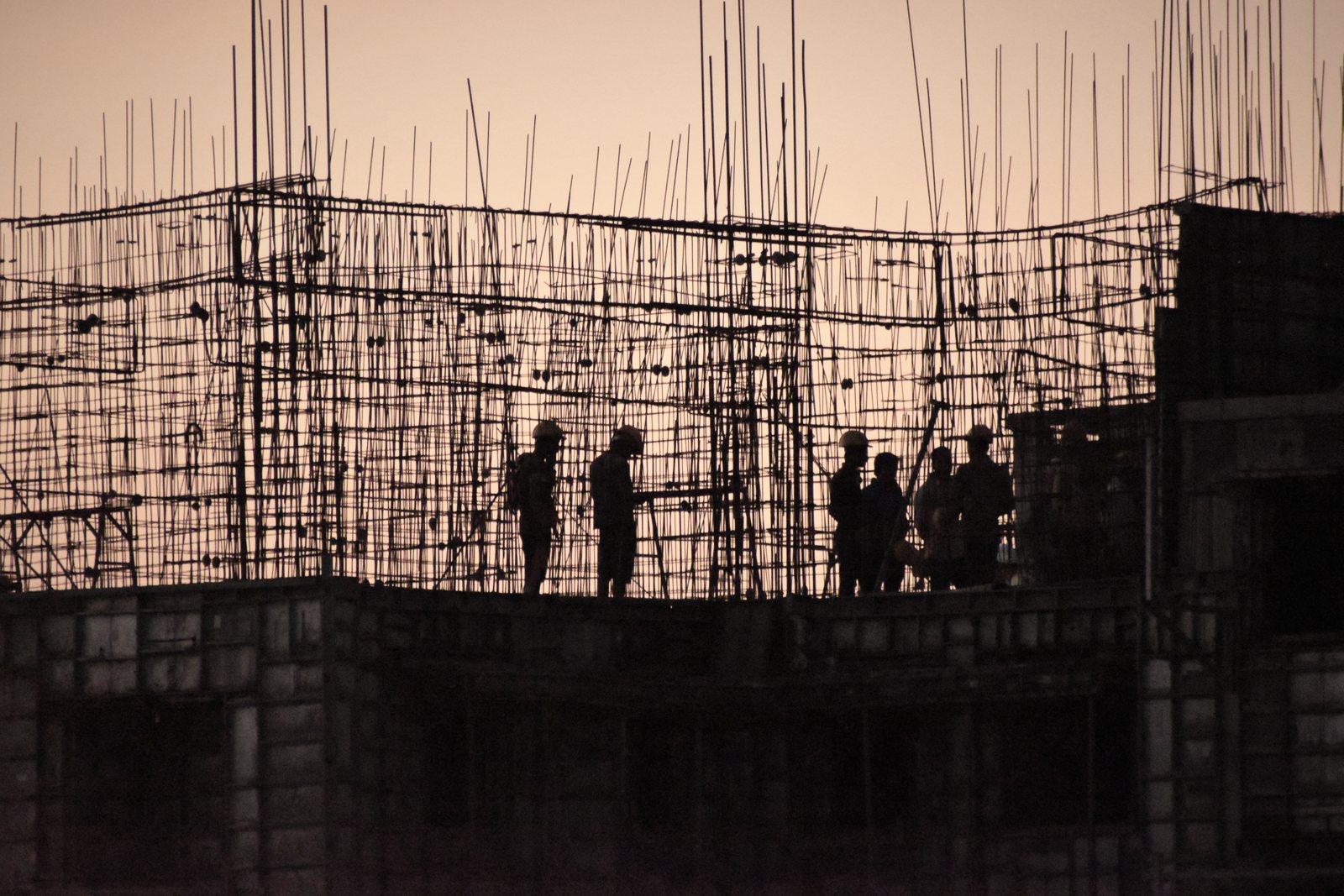 Silhouettes de compagnons casqués sur un plancher hérissé d'armatures en attente, au crépuscule, photo d'illustration
